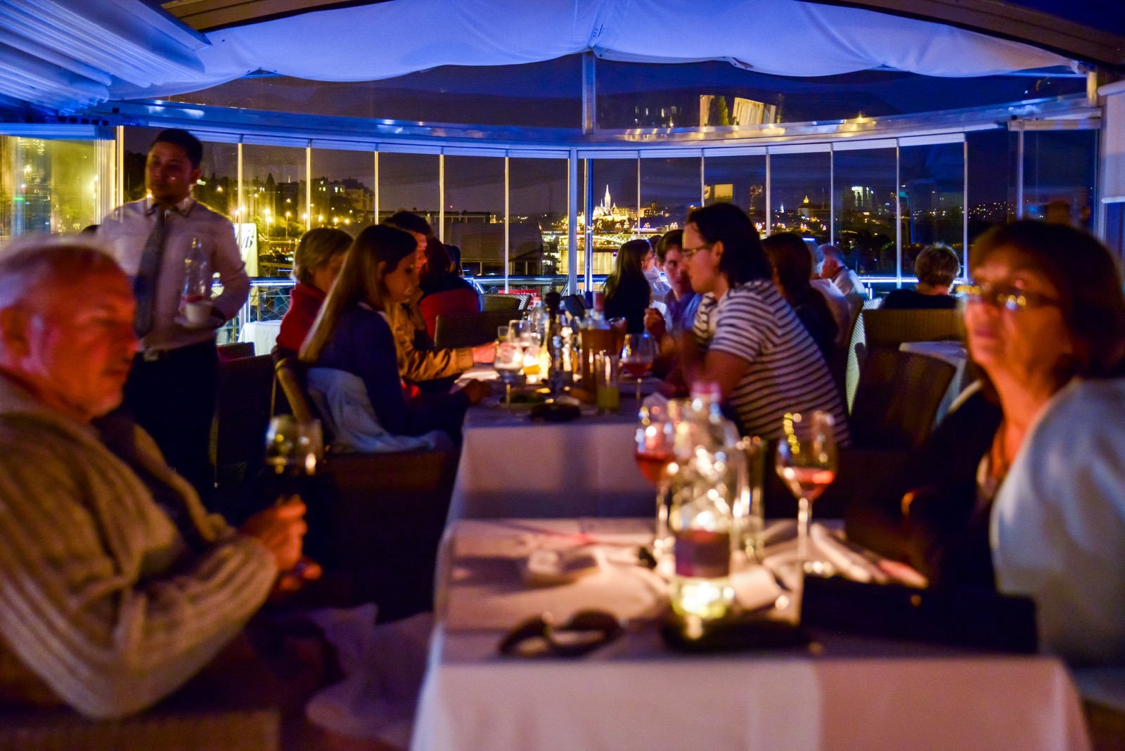 Guests at dinner in the evening, the illuminated riverbank behind them